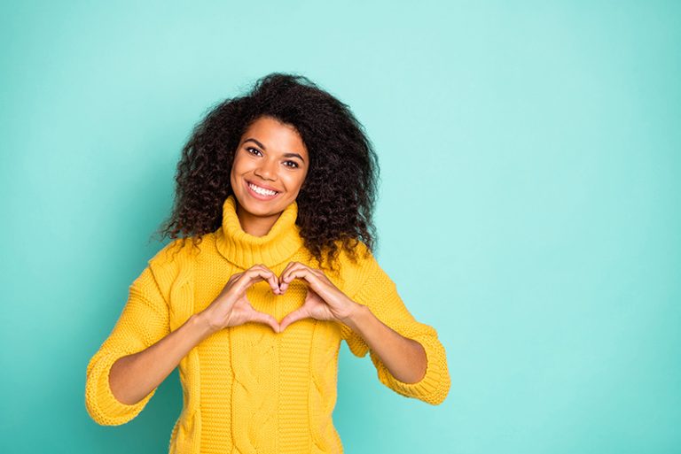 A woman smiling and making a love heart shape with her hands