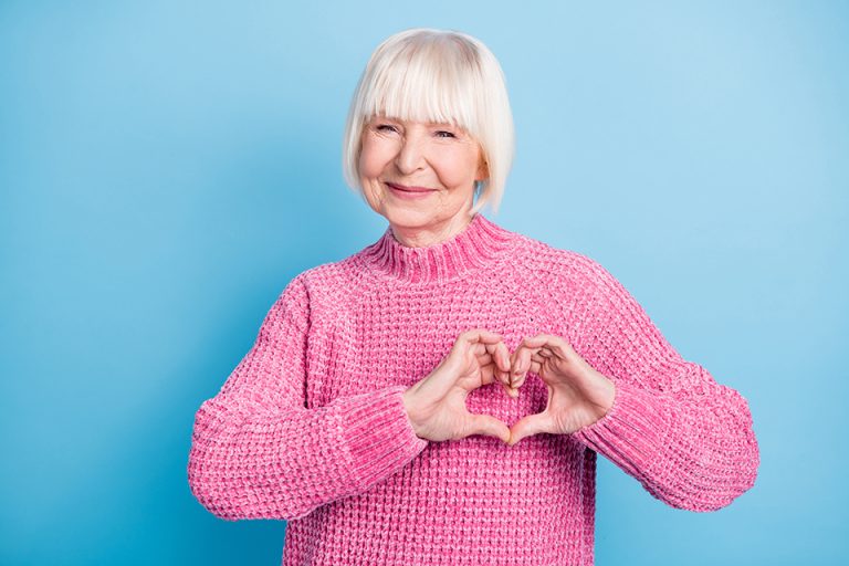 Happy woman in a pink jumper making a heart shape with her hands