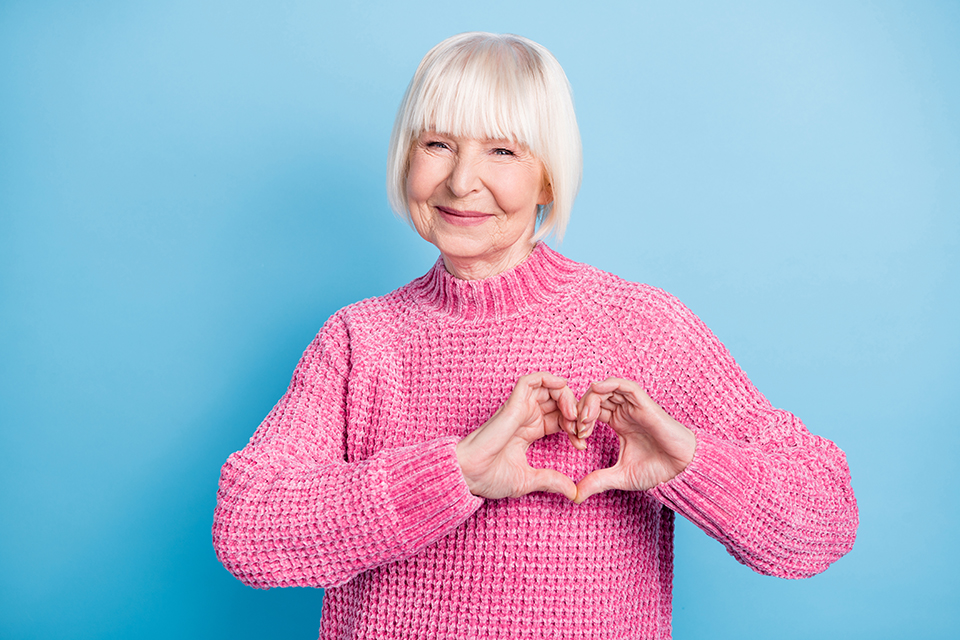 Happy woman in a pink jumper making a heart shape with her hands