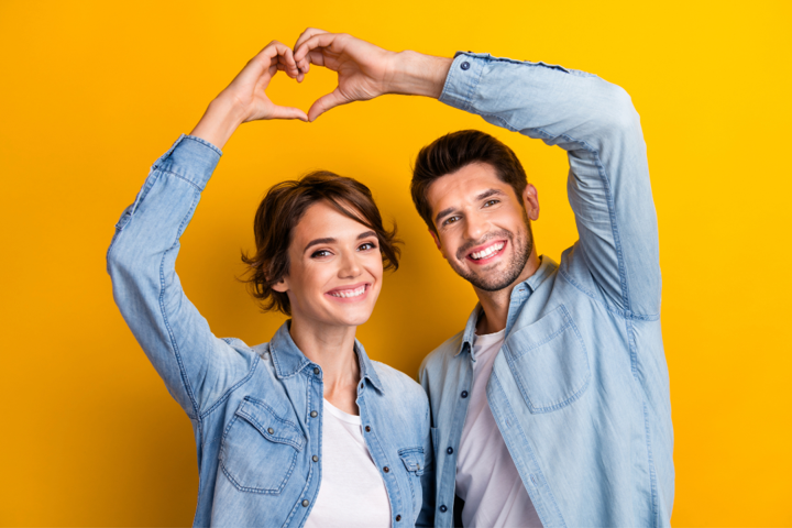 Happy man and woman smiling and making a heart sign with their hands.